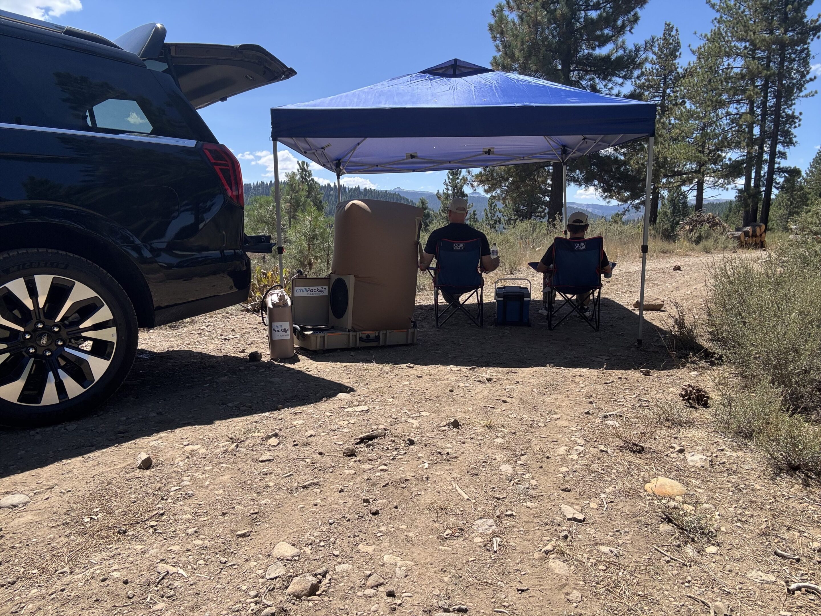 Two people under blue canopy at campsite