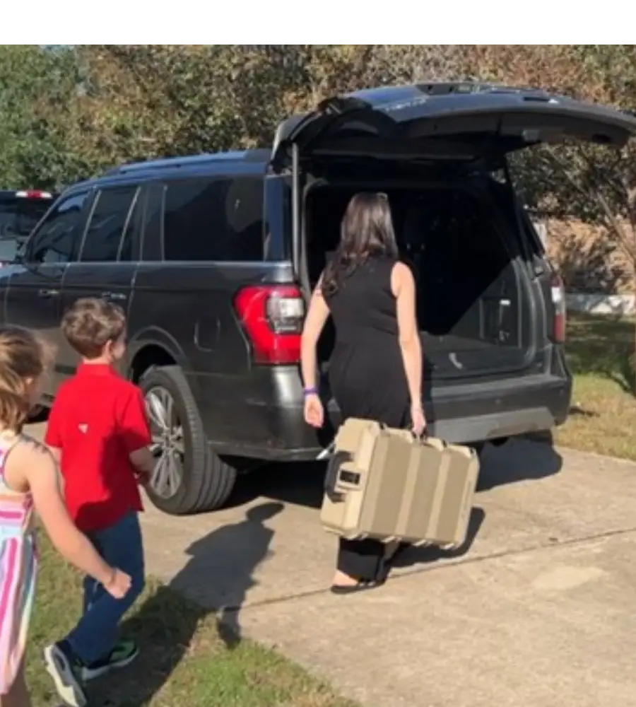 Woman loading suitcase into SUV, children watching