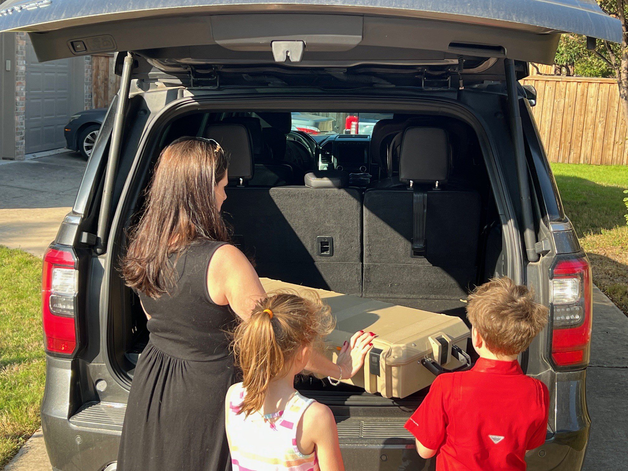 Family loading suitcase into SUV trunk